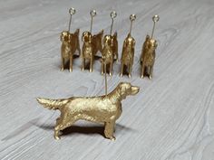 golden dog figurines lined up on a white wood floor with pins in the shape of people