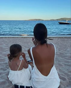 two women sitting on the beach looking out at the water