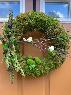 a moss wreath with two birds sitting on top of it, hanging from the side of a door