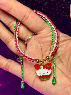 a hand holding a hello kitty bracelet with red, white and green beads on it