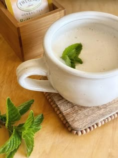 a white cup filled with liquid sitting on top of a wooden table next to green leaves