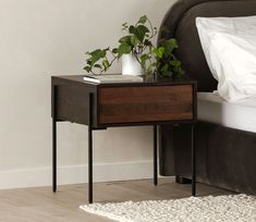 a nightstand with a plant on top of it next to a white pillow and bed