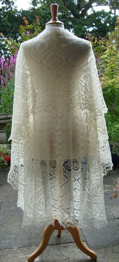 a white crocheted shawl on a wooden stand in front of some flowers