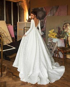 a woman in a white wedding dress standing on a wooden floor with her back to the camera