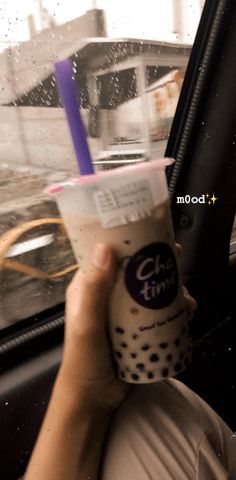 a woman holding up a cup of coffee in the back seat of a car on a rainy day