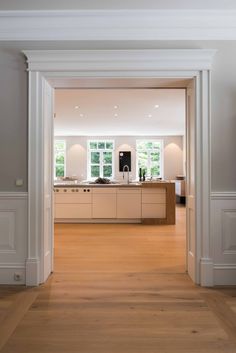 an open door leading to a kitchen and living room with white walls, wood floors and cabinets