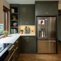 a kitchen with green cabinets and stainless steel refrigerator freezer combo in the center, along with wooden flooring