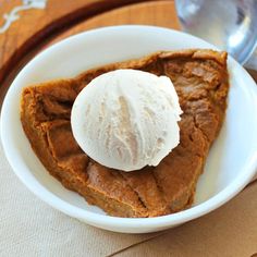 a slice of pumpkin pie with ice cream in a white bowl on a wooden table