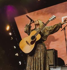 a woman singing into a microphone and holding a guitar in her hand while standing on stage