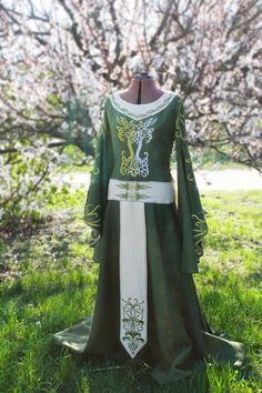 a green dress with white trims and an elaborate design on the front, sitting in grass