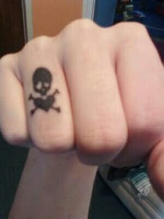 a person with a skull and crossbone tattoo on their finger