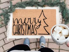 someone is holding a coffee cup in front of a door mat with merry christmas written on it