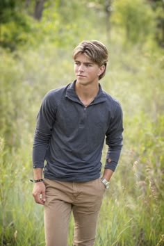 a young man standing in the middle of a field with his hands in his pockets