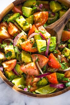 a wooden spoon in a bowl filled with chopped tomatoes and avocado salad dressing