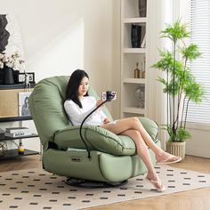 a woman sitting in a green chair holding a camera and looking at her cell phone