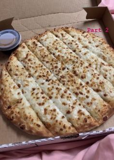 a pizza sitting in a box on top of a pink blanket next to a cup