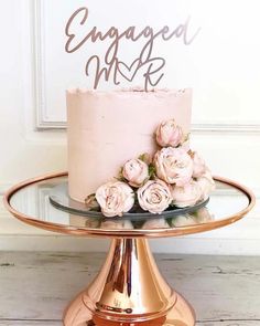 a pink cake with flowers on top sitting on a gold stand next to a white door