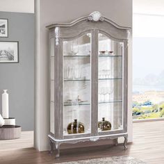 a white china cabinet with glass doors and shelves in the middle of a living room