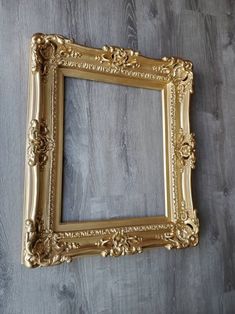 an ornate gold frame on a wooden wall with wood flooring and grey walls in the background