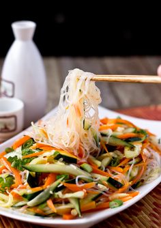 a white plate topped with veggies and chopsticks next to a cup