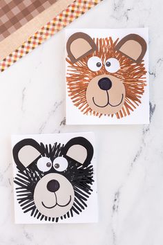 two cards with animal faces on them sitting on a marble surface next to a brown and white checkered table cloth