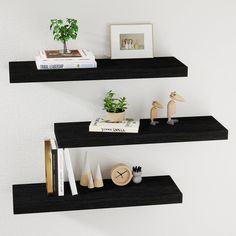 two black floating shelves with books, plants and other items on them in a white room