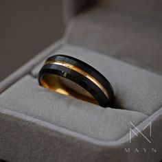 a black and gold wedding band sits in a velvet ring box with its lid open