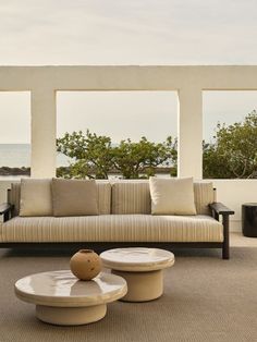 a living room with two couches and tables in front of large windows overlooking the ocean