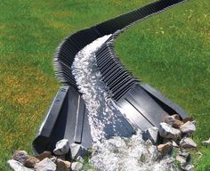 water flowing out of a drainage pipe into a stream in the grass next to some rocks