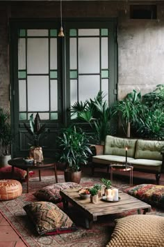 a living room filled with lots of plants next to a couch and table in front of two windows