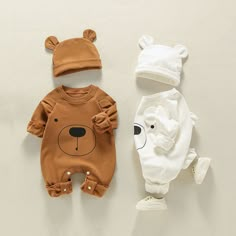 three baby clothing items laid out on a white surface, including a bear onesuit and a teddy bear hat