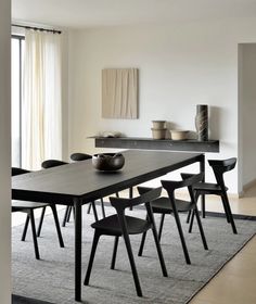 a dining room table with chairs and a bowl on it in front of a window