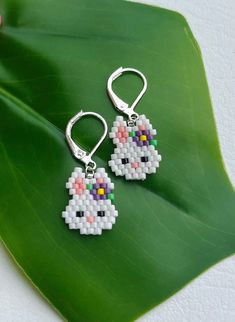 a pair of earrings that have been made to look like a cat on a green leaf