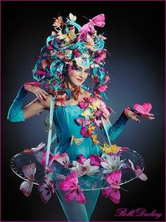 a woman dressed in blue and pink with butterflies on her head, holding a butterfly shaped object