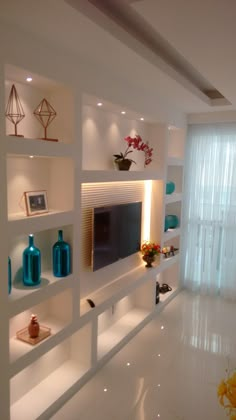 a living room filled with lots of white shelves next to a wall mounted flat screen tv