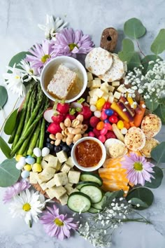 a platter filled with cheese, crackers, and veggies next to flowers