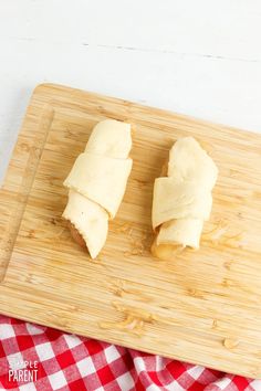 two pieces of bread sitting on top of a wooden cutting board next to a red and white checkered cloth