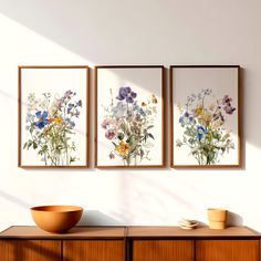 three framed pictures on the wall above a wooden cabinet with a bowl and plate sitting on it