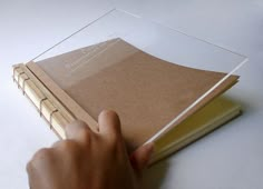 a person is holding a book in front of a clear cover on a white table