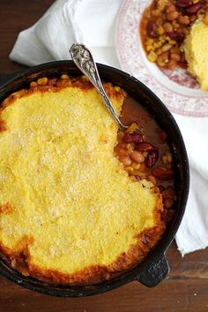 a skillet filled with baked beans and corn next to a bowl of cornbread