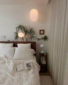 a bed with white sheets and pillows in a bedroom next to a potted plant