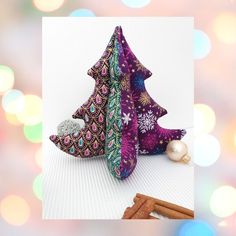 two christmas trees made out of fabric and some cinnamon sticks on a white surface with colorful lights in the background