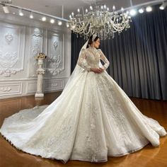 a woman in a white wedding dress standing on a wooden floor next to a chandelier