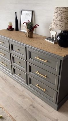 a grey dresser with gold handles and knobs in a room next to a lamp