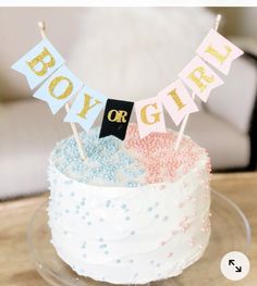 a white cake topped with blue and pink sprinkles on top of a wooden table