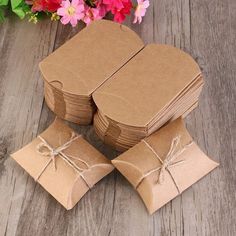 several pieces of brown paper tied with twine on wooden table next to pink flowers