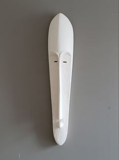 a white mask hanging on the wall next to a gray wall with one eye closed