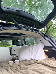 an open car trunk with pillows and coffee cups in the bed area, on a sunny day