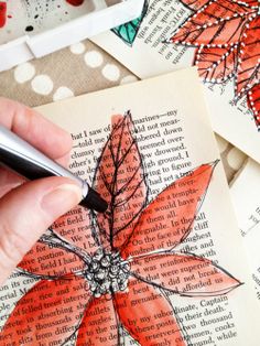 a person holding a pen and writing on top of an open book with red flowers