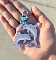 a hand holding a plastic keychain with two dolphins on it